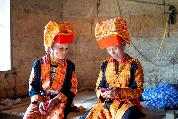 Two Women Wearing Traditional Dao Lu Gang Minority Clothing Using A Smart Phone