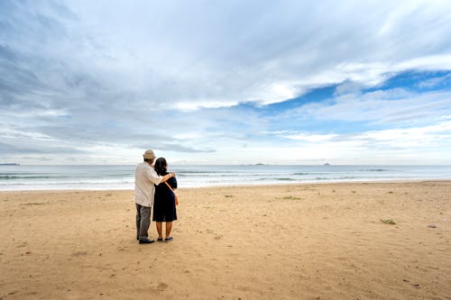 Back View of a Senior Couple Standing on a Sandy Beach and Looking at Sea