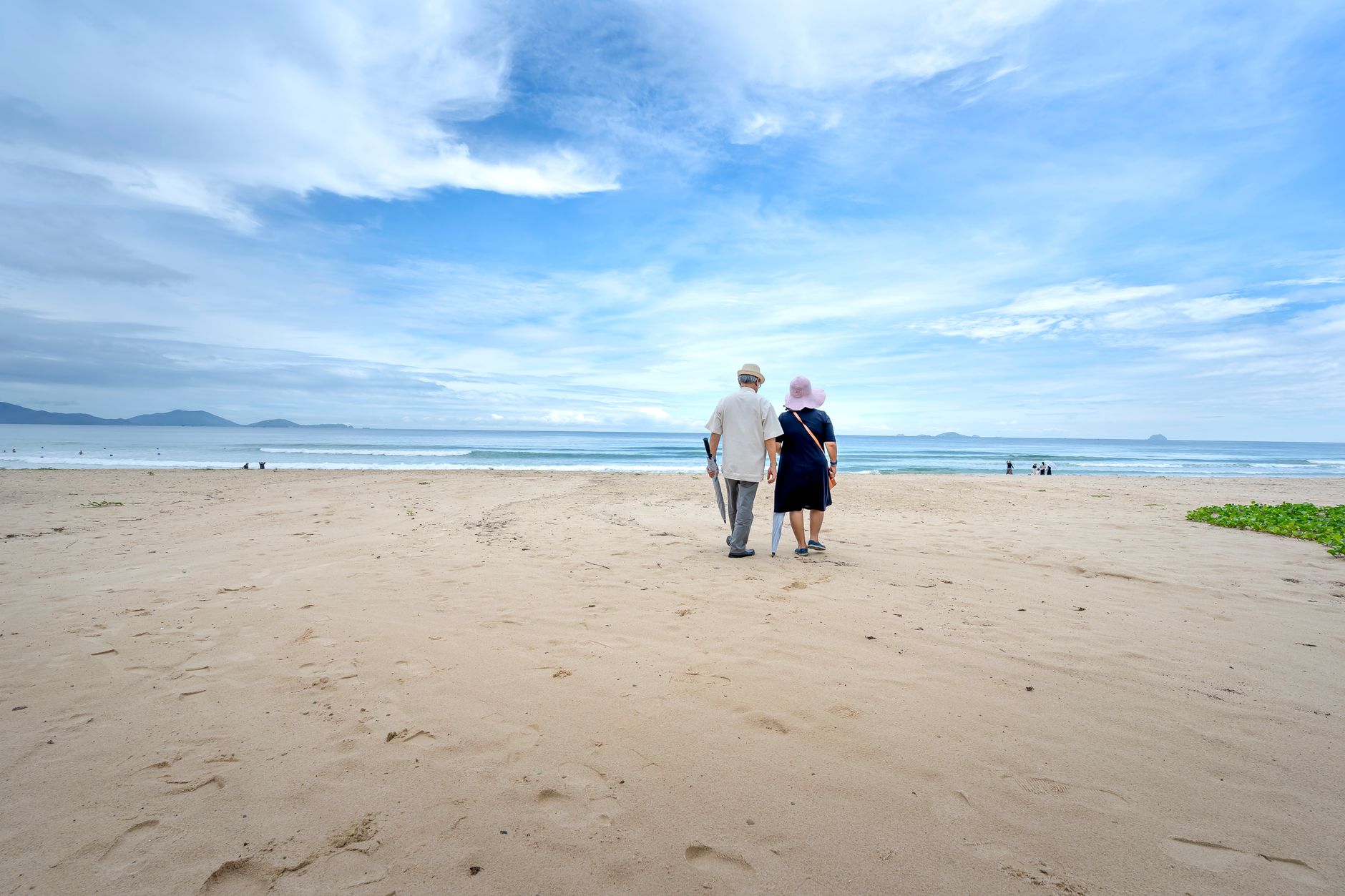 A senior couple walking on a serene sandy beach under a beautiful cloudy sky.