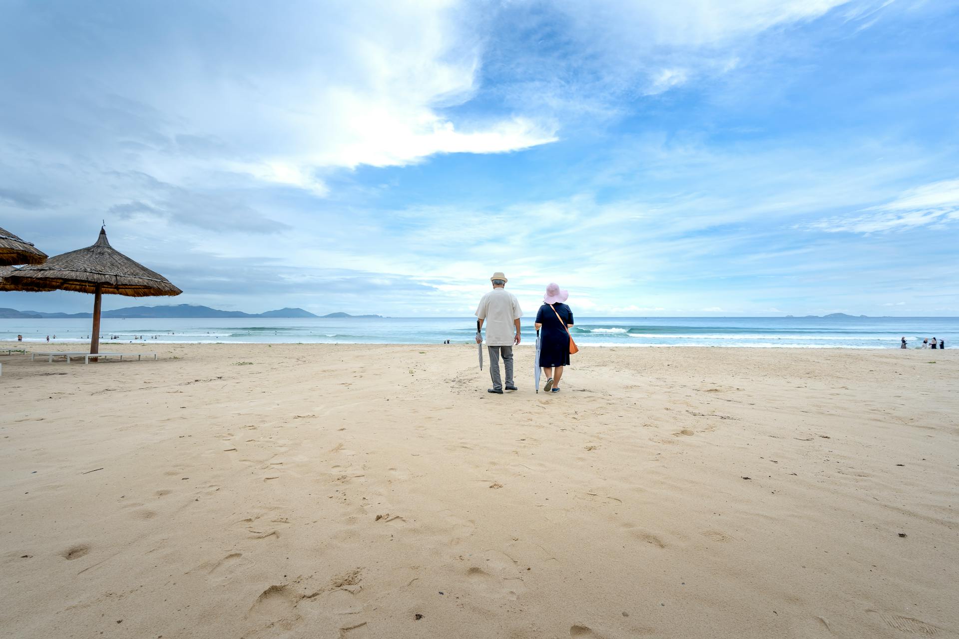 Senior couple enjoying a peaceful walk on a sandy beach under a wide blue sky.