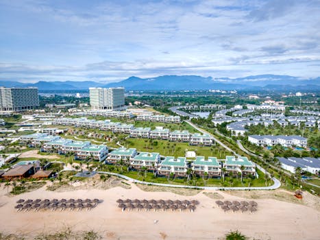 Aerial shot of a beach resort with villas and mountain backdrop, perfect for summer vacations.