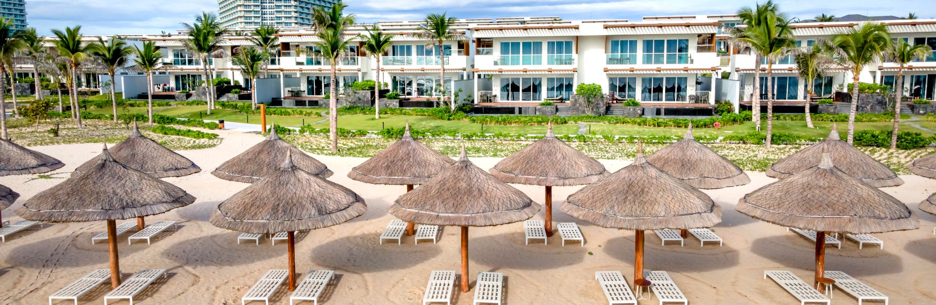 A serene beachside view with straw umbrellas and a luxury resort backdrop.