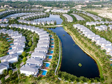 Stunning aerial view of tropical villas with pools overlooking a serene lagoon, ideal for vacation and leisure.