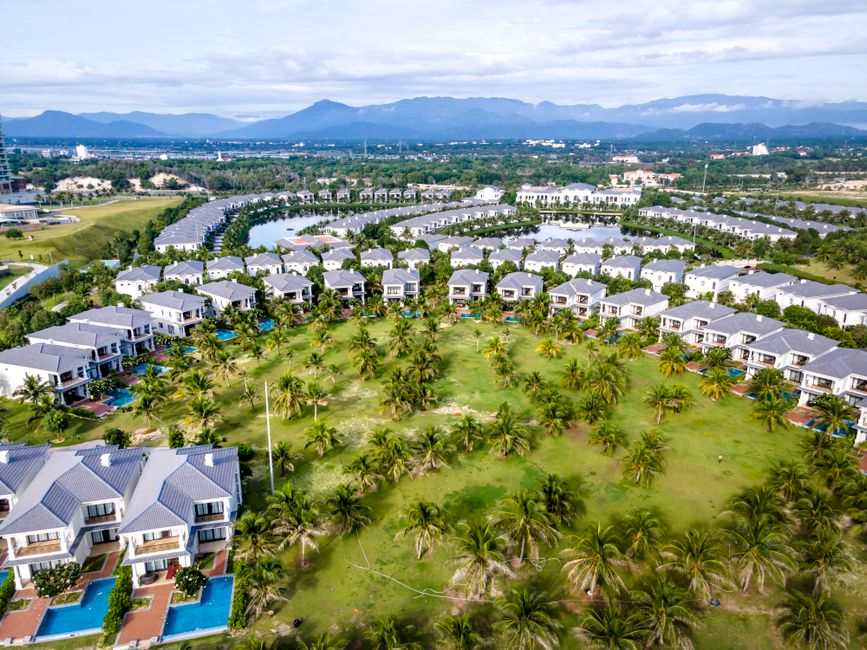 Aerial shot of a tropical resort with villas surrounded by palm trees.