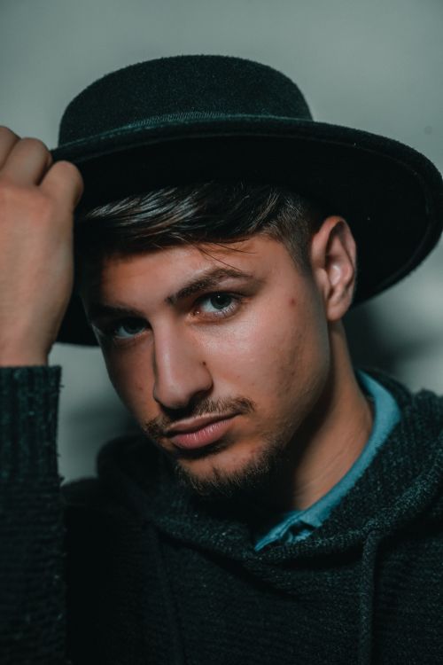 Free Fashionable portrait of a man wearing a black fedora hat and sweater, striking a serious pose. Stock Photo