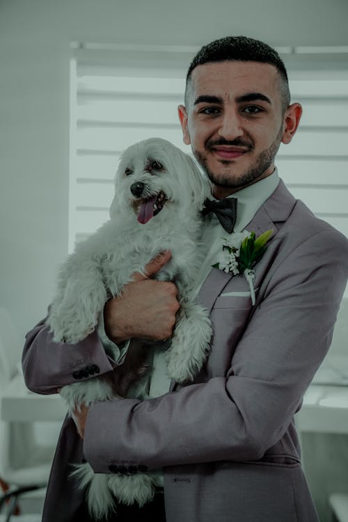 Photo of a Man in a Suit Holding a White Dog
