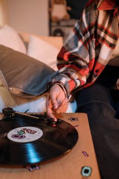 Person playing a vintage vinyl record on a turntable indoors, wearing plaid.