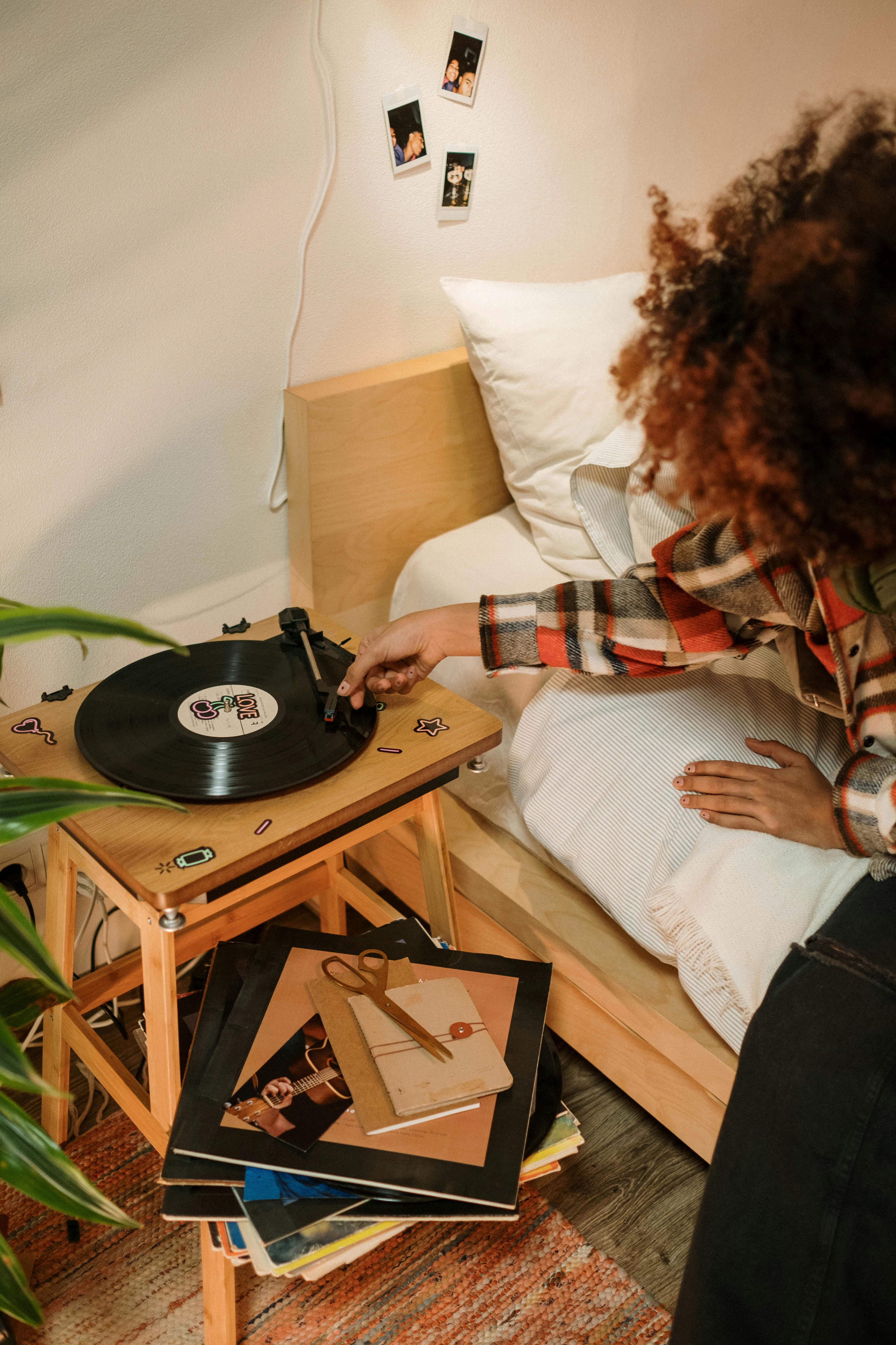 Person playing a vinyl record in a cozy bedroom with warm decor.