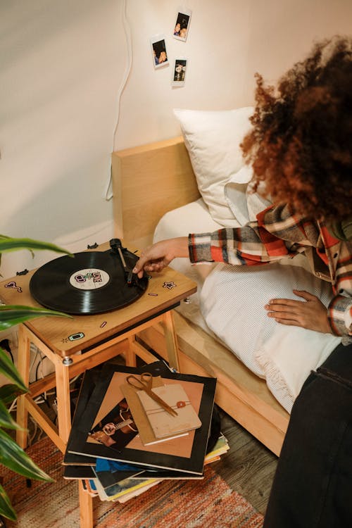A Person Sitting on the Bed Touching the Spinning Vinyl Record on a Turntable