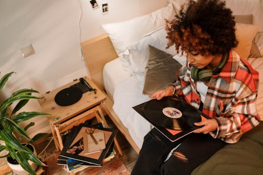 A woman sitting on bed, holding a vinyl record with headphones in a cozy room.