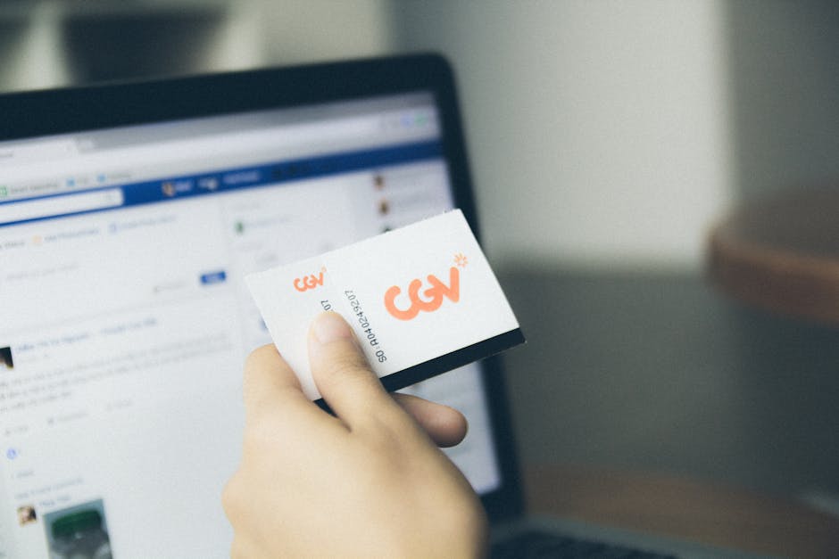 Close-up of a hand holding a card near an active laptop screen, indoors.