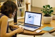 一位女士在家远程工作，办公桌上摆放着笔记本电脑、笔和植物，展现了数字游牧的生活方式