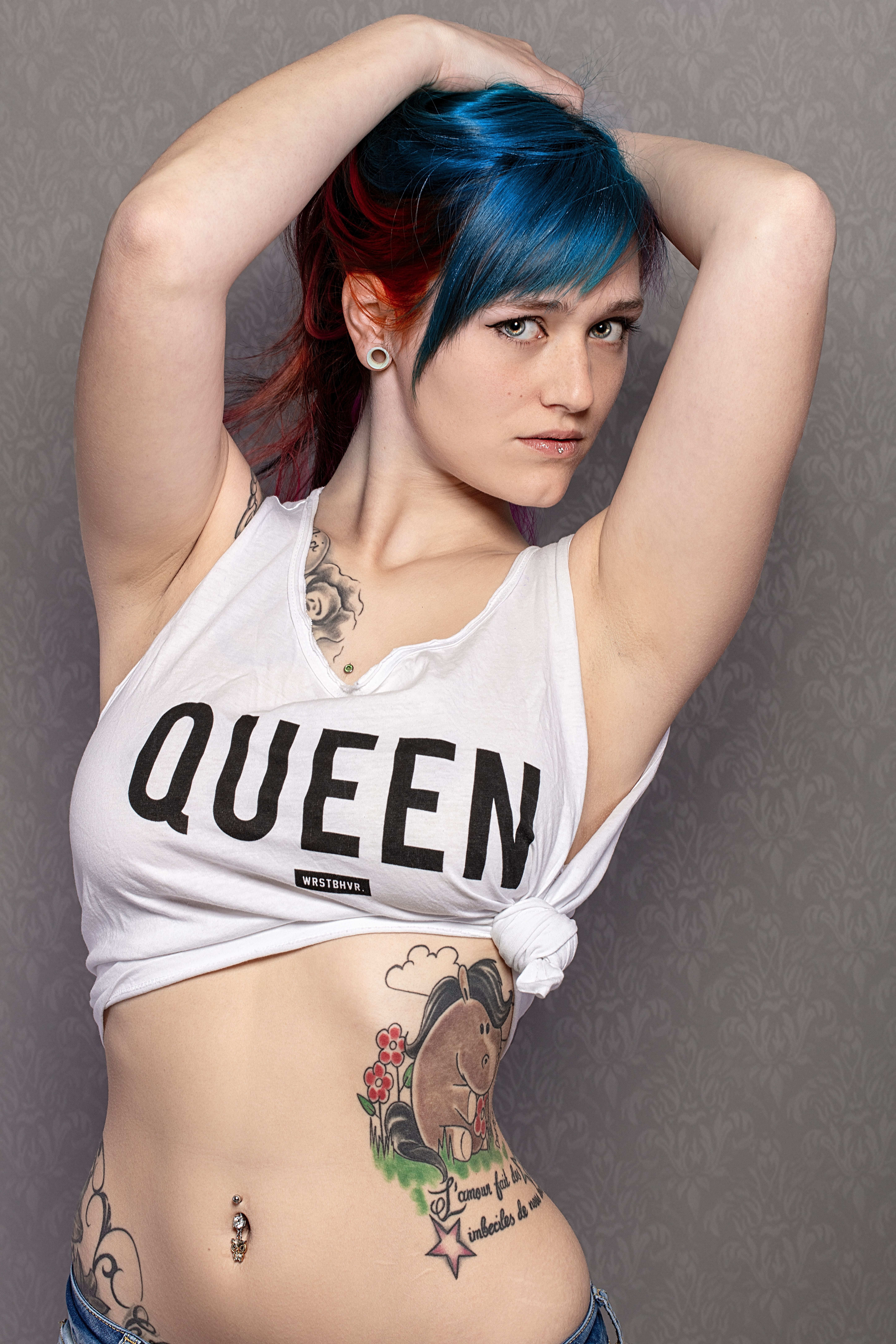 Portrait of a stylish woman with blue hair and tattoos posing confidently indoors.