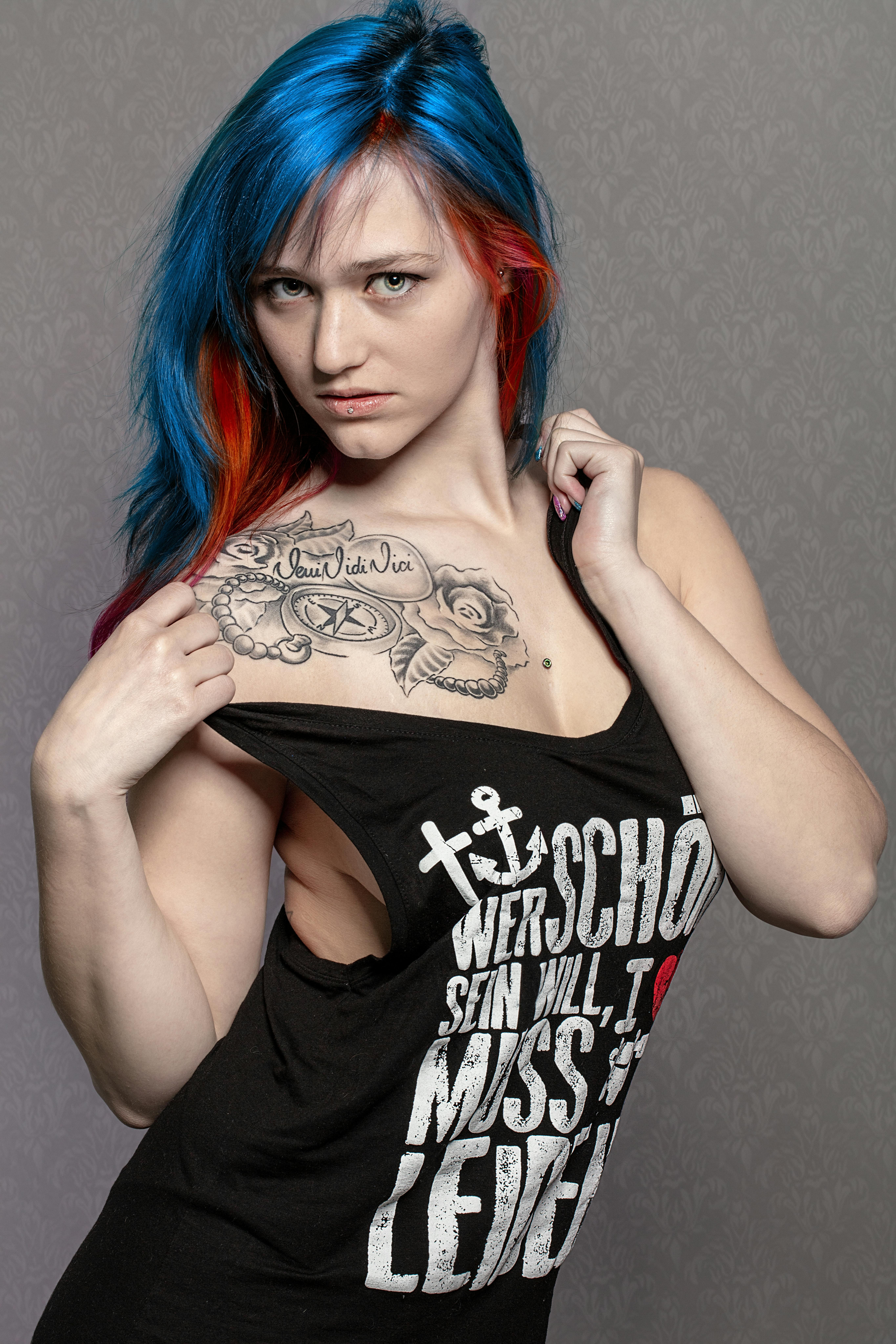 Studio portrait of a young woman with colorful dyed hair and tattoos, wearing a black tank top.