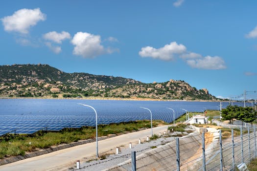 A vast solar farm with solar panels under a bright blue sky and mountainous landscape.