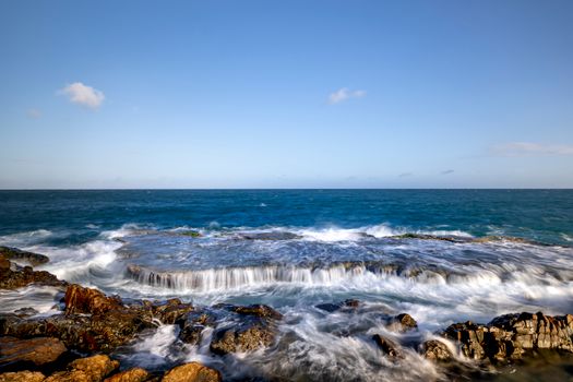 Captivating view of the ocean's crashing waves against a rocky shore under a clear blue sky.