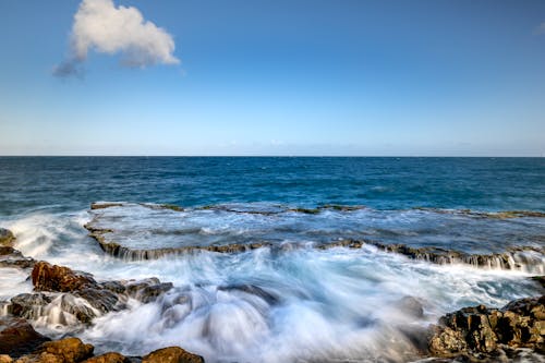 Blue Seascape with Waves on Rocks and Cloud in Sky