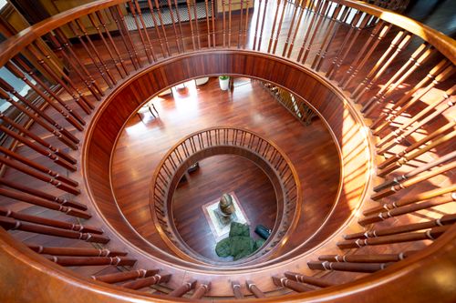 Free View from above of a stunning wooden spiral staircase lit by natural sunlight, showcasing elegant interior design. Stock Photo
