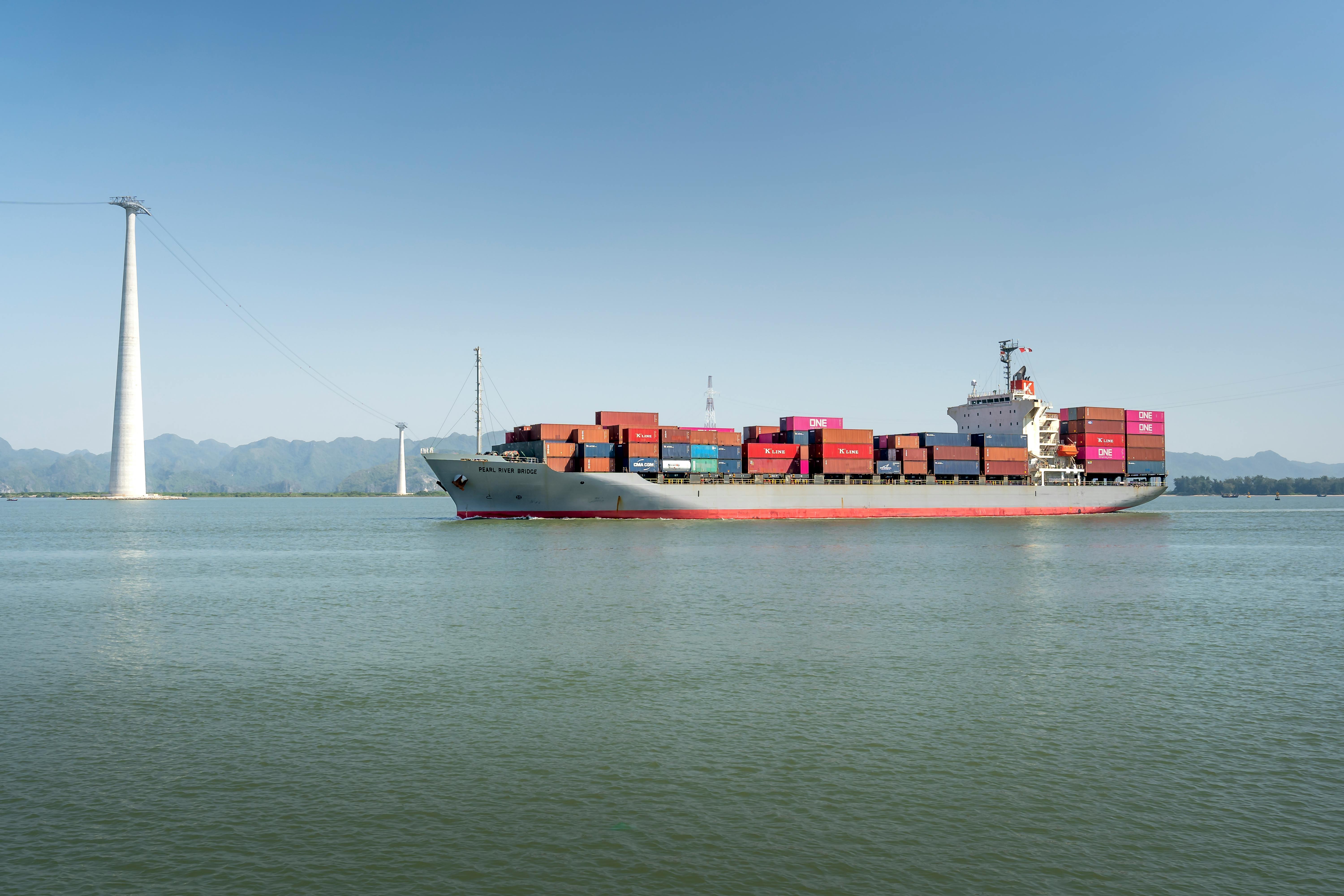 Free A large cargo ship carrying colorful containers sails smoothly across a calm ocean on a clear sunny day. Stock Photo
