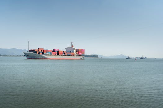 A large cargo ship travels across the open ocean, framed against distant mountains under a clear sky.