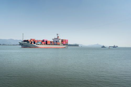 Free A large cargo ship travels across the open ocean, framed against distant mountains under a clear sky. Stock Photo
