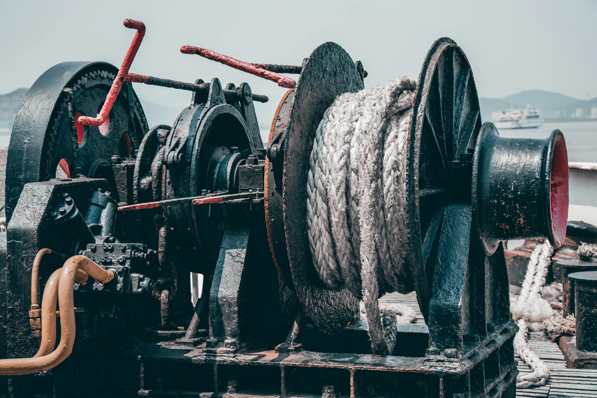 A close-up view of an industrial hydraulic winch on a ship deck with ropes.