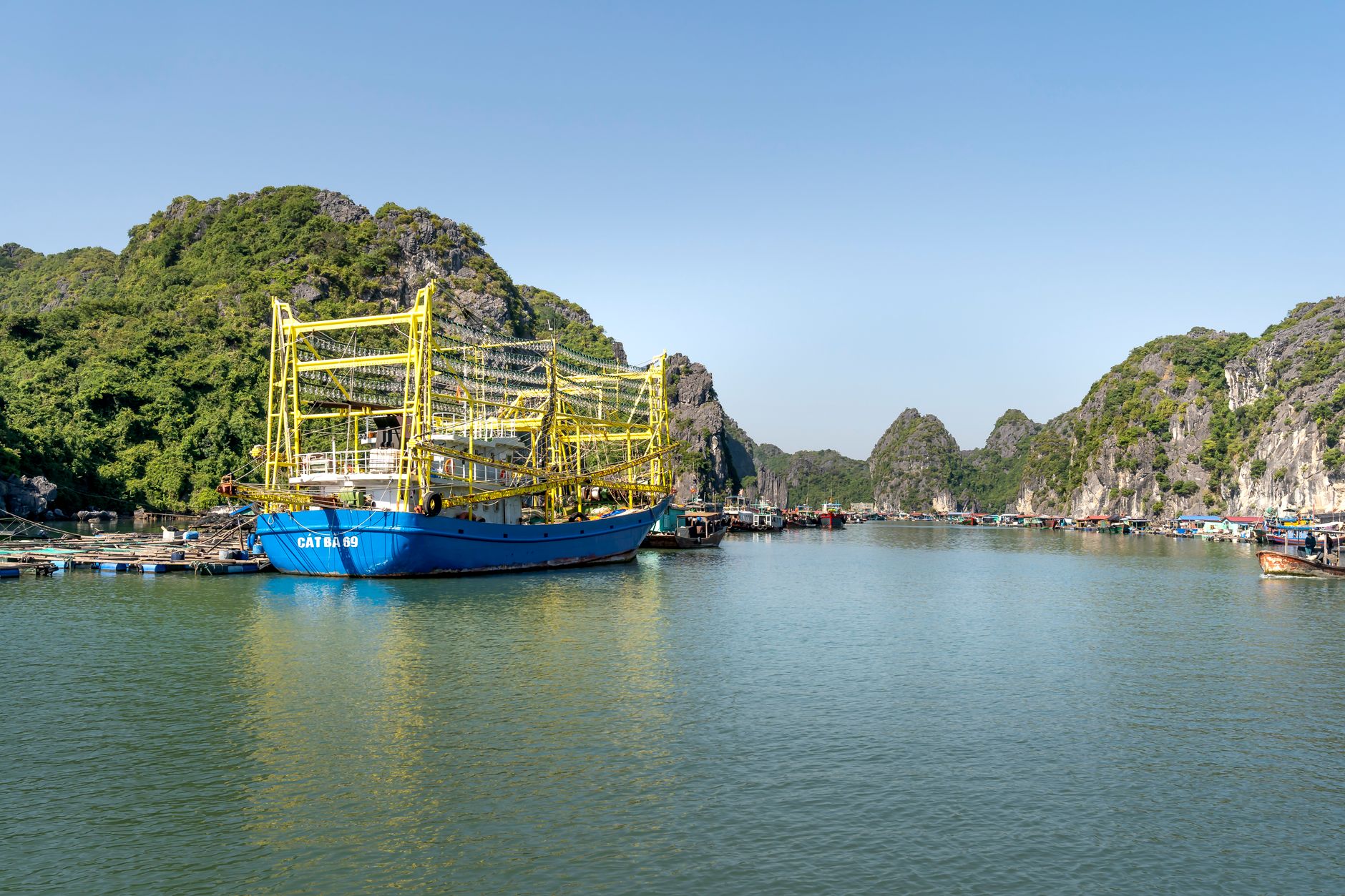 A vibrant fishing boat moored in a picturesque Vietnamese harbor, surrounded by lush hills.