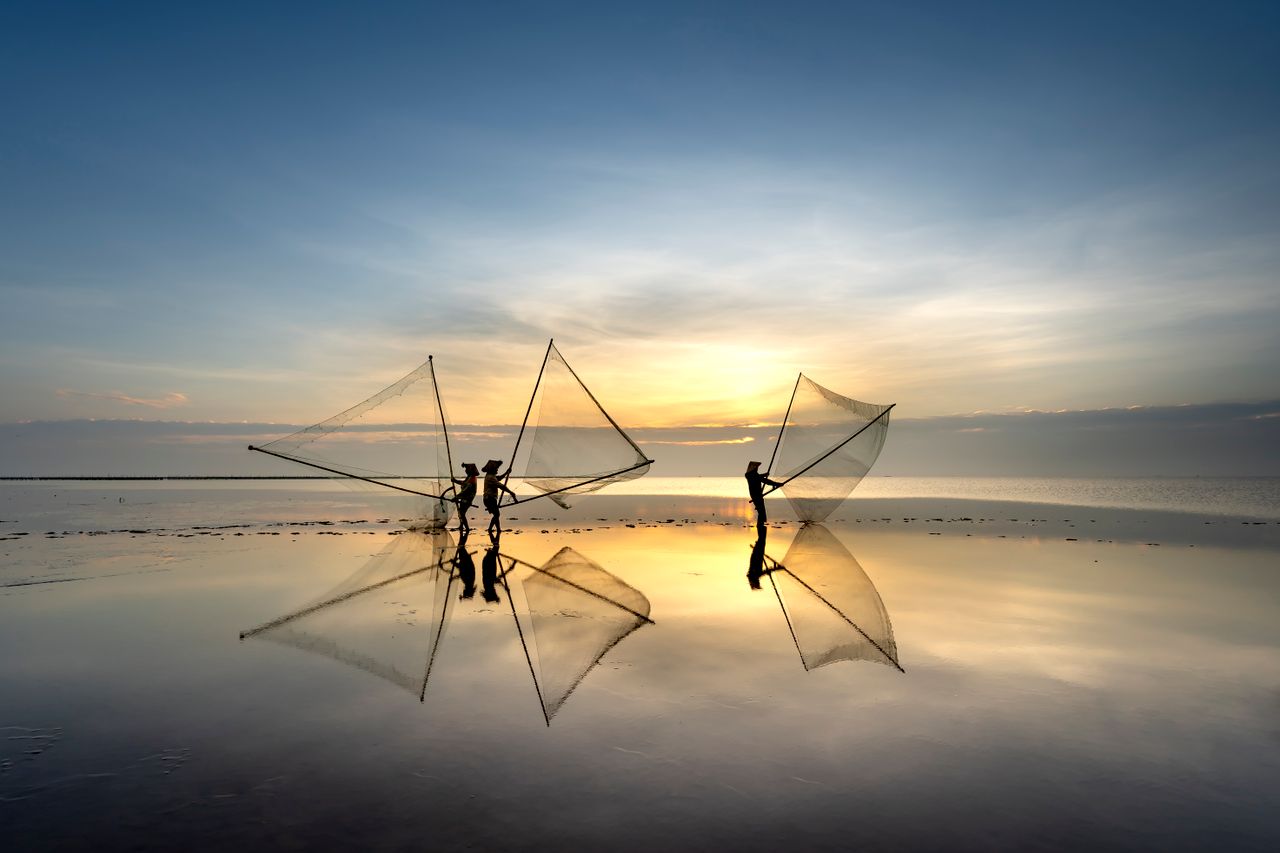 silhouetted fishermen cast nets in serene sunrise reflection on calm s