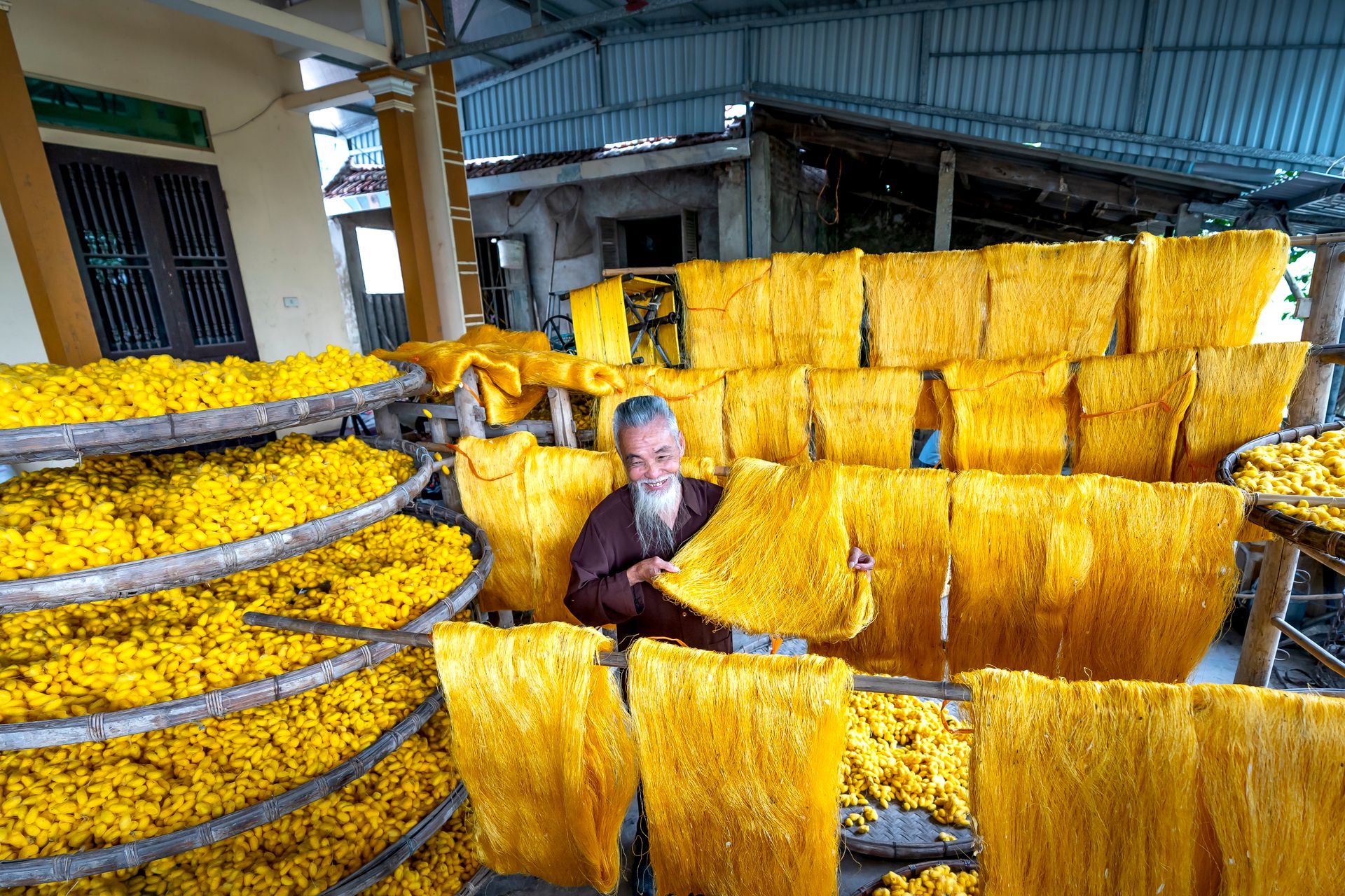 An experienced worker processes yellow silk threads in an indoor production facility.
