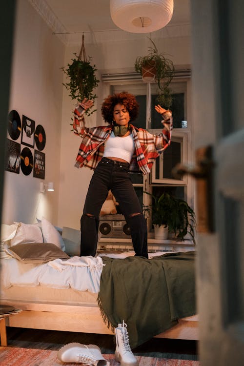 Woman in White and Red Long Sleeve Shirt and Black Denim Jeans Dancing on Bed