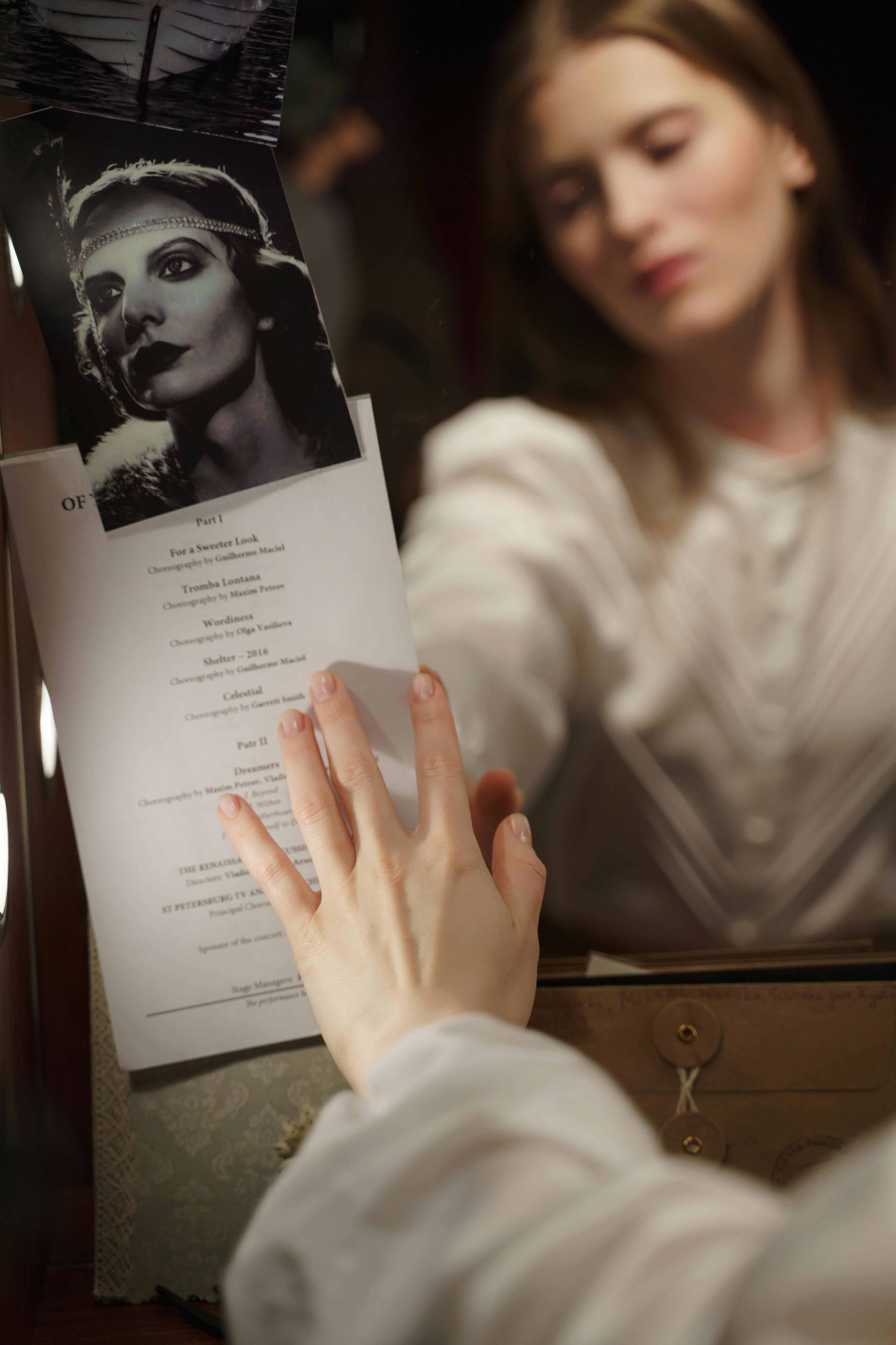 woman in white long sleeve shirt holding a script in front of mirror