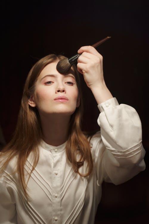 Woman in White Button Up Long Sleeve Shirt Doing Makeup