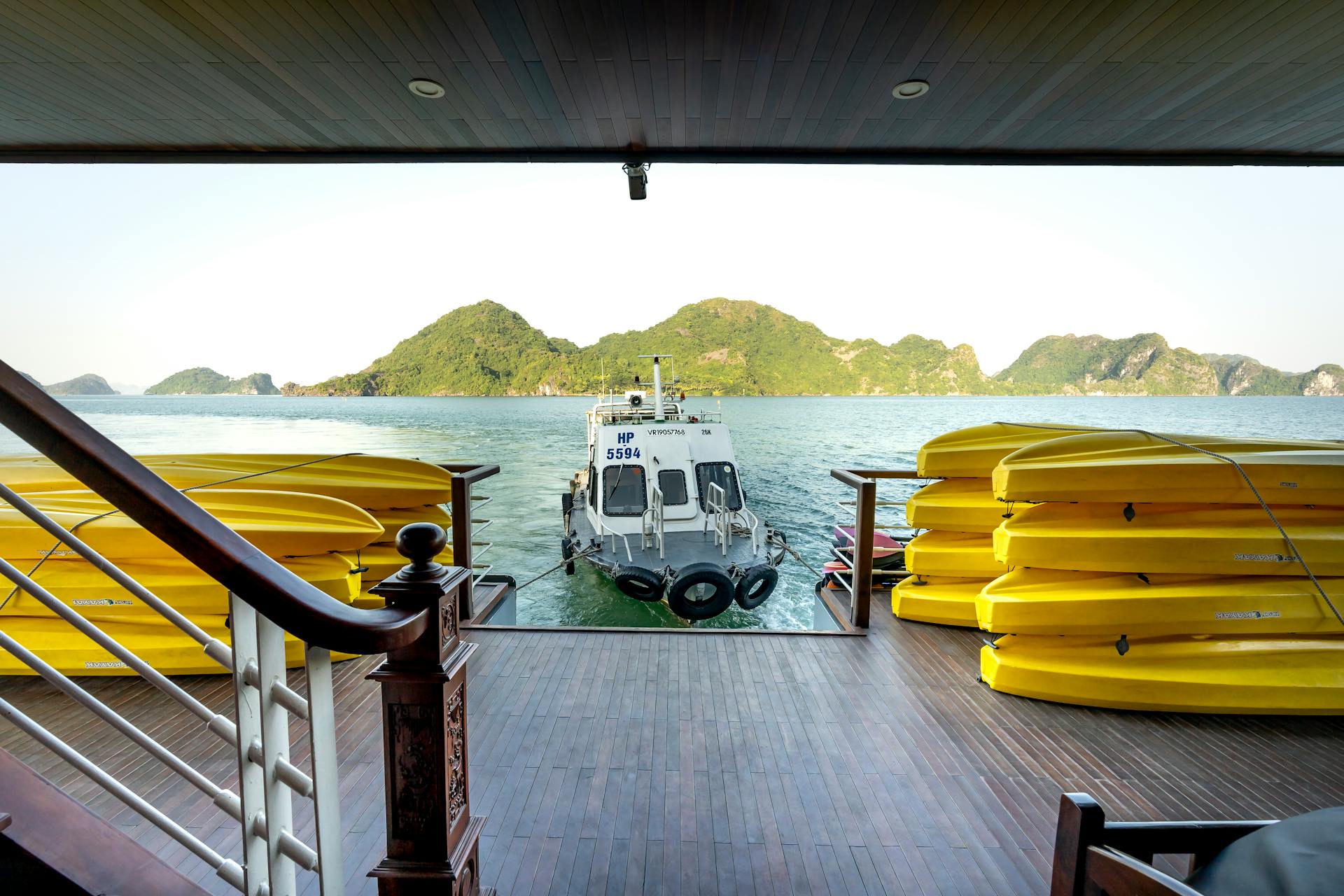 A serene view of a boat docking at a tropical island surrounded by kayaks and lush hills.