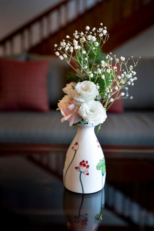 Free Delicate white flowers arranged in a beautiful ceramic vase on a glass coffee table, creating a serene indoor ambiance. Stock Photo