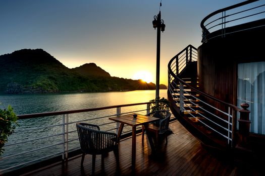 Experience a serene sunset from a ship deck with ocean view and mountains.