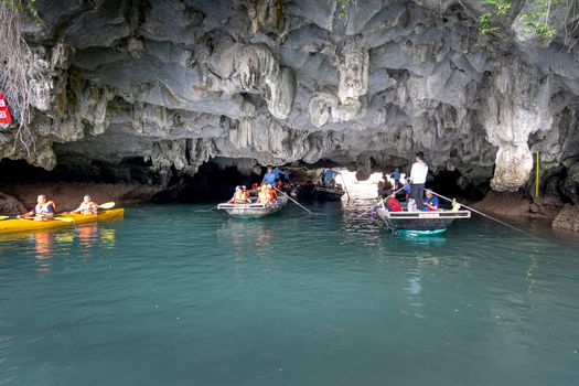 Tourists explore stunning cave formations by boat and kayak in a serene waterway.