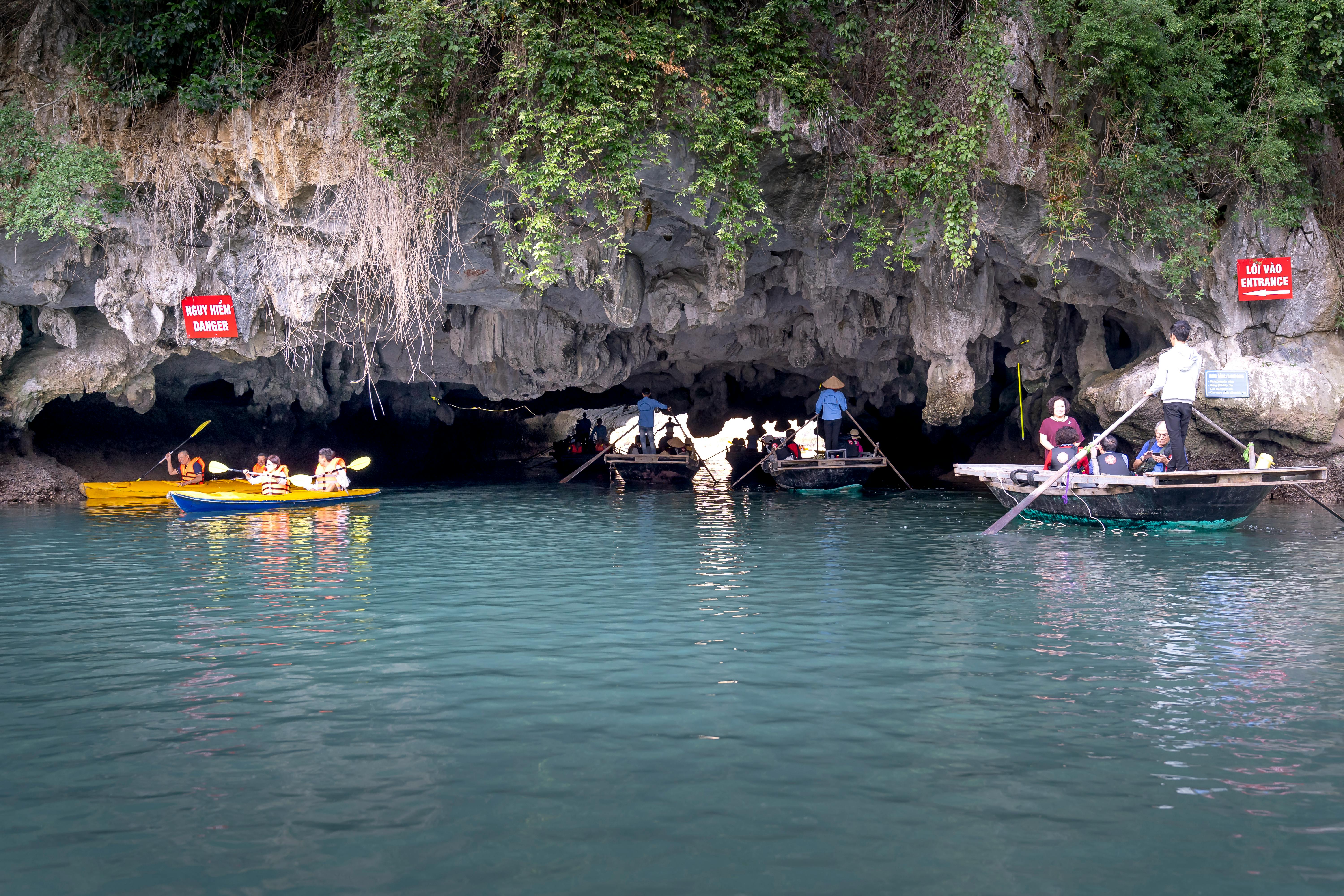 Kayakers and tourists navigate through a picturesque limestone cave entrance on a tranquil day.
