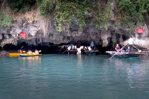 Kayakers and tourists navigate through a picturesque limestone cave entrance on a tranquil day.