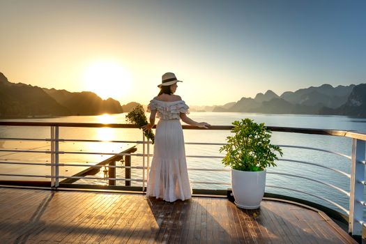 A woman in a white dress and hat gazes at the ocean during sunset, creating a serene and picturesque scene.