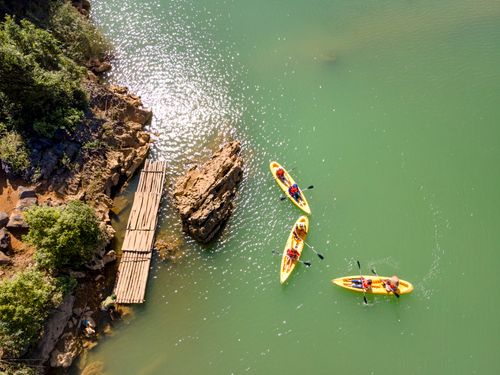 Free Aerial shot of three kayaks with people paddling near a rocky shore and an old wooden pier. Stock Photo