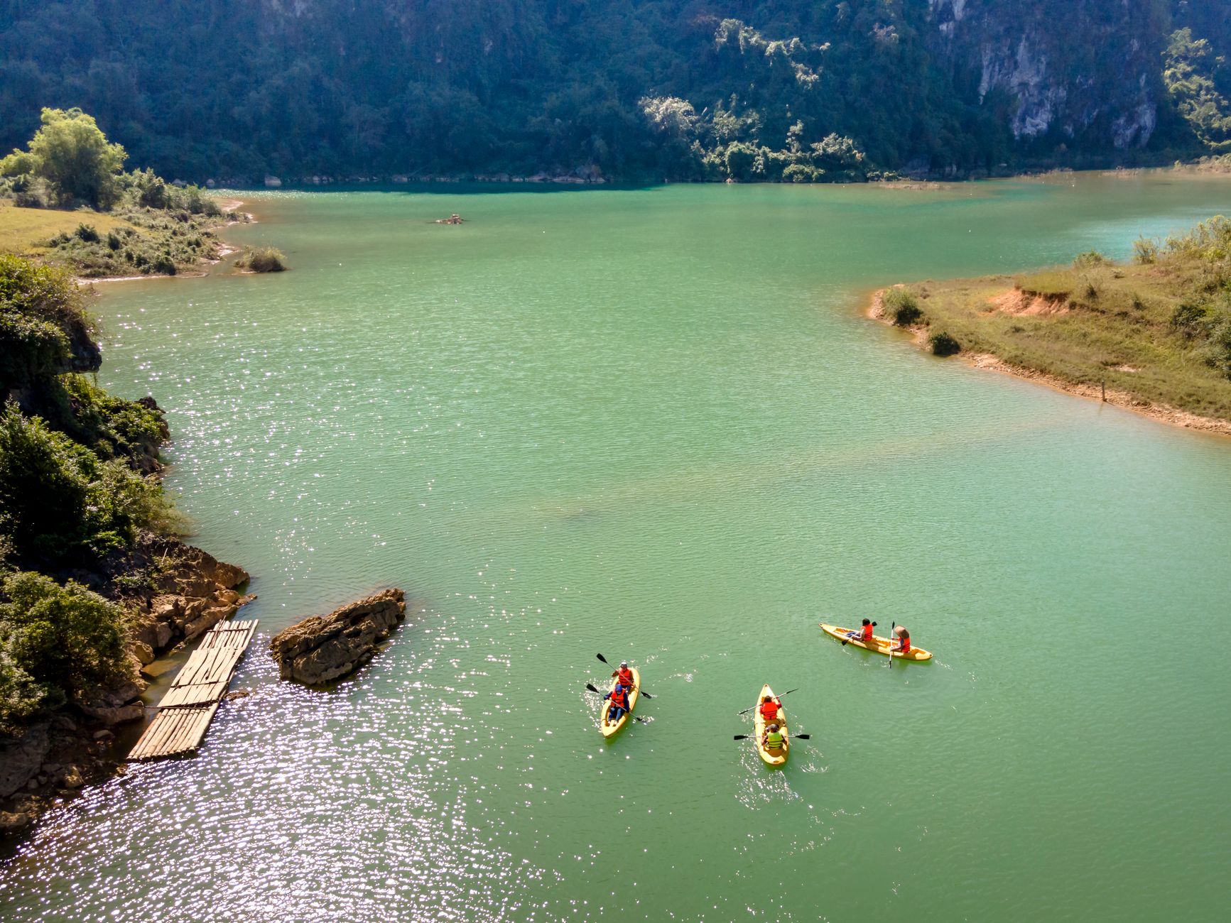 Three kayakers enjoy a peaceful paddle on a tranquil turquoise lake surrounded by lush greenery.