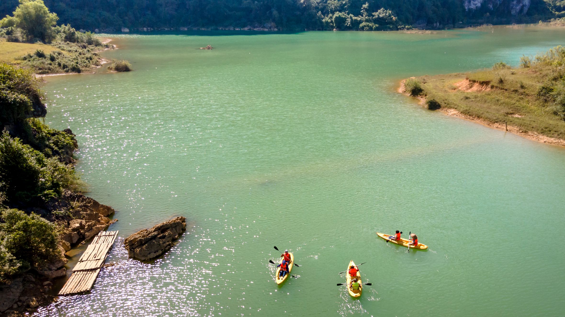 Three kayakers enjoy a peaceful paddle on a tranquil turquoise lake surrounded by lush greenery.