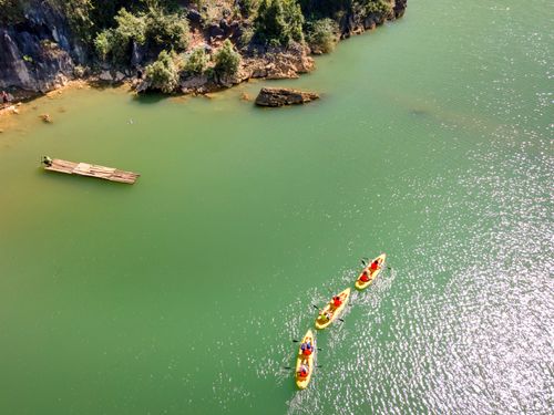 Free Aerial shot of people canoeing on serene green waters near a rocky shoreline. Stock Photo