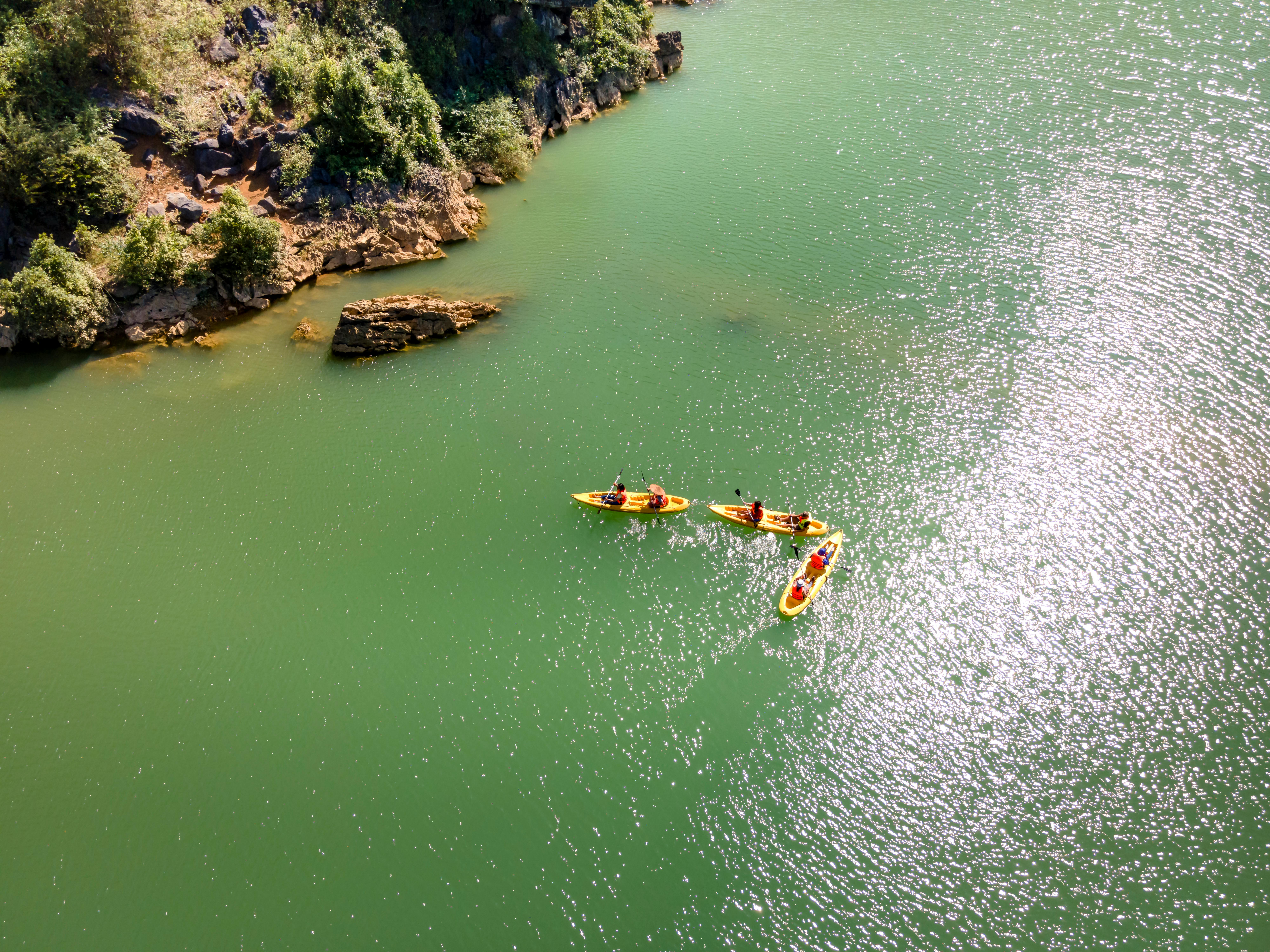 Three kayaks paddling along a scenic green river, surrounded by rocky cliffs.