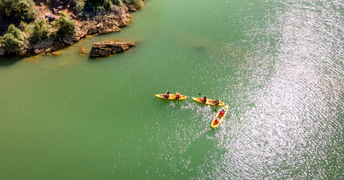 Three kayaks paddling along a scenic green river, surrounded by rocky cliffs.