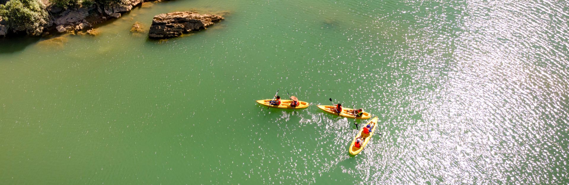 Three kayaks paddling along a scenic green river, surrounded by rocky cliffs.