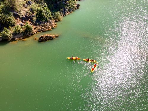 Free Three kayaks paddling along a scenic green river, surrounded by rocky cliffs. Stock Photo