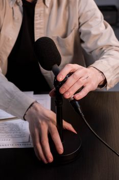 Person adjusting a microphone on a stand, readying for a podcast or recording session indoors.