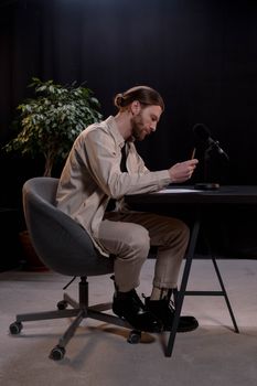 Caucasian man sitting and writing at a desk with a microphone for podcast recording.