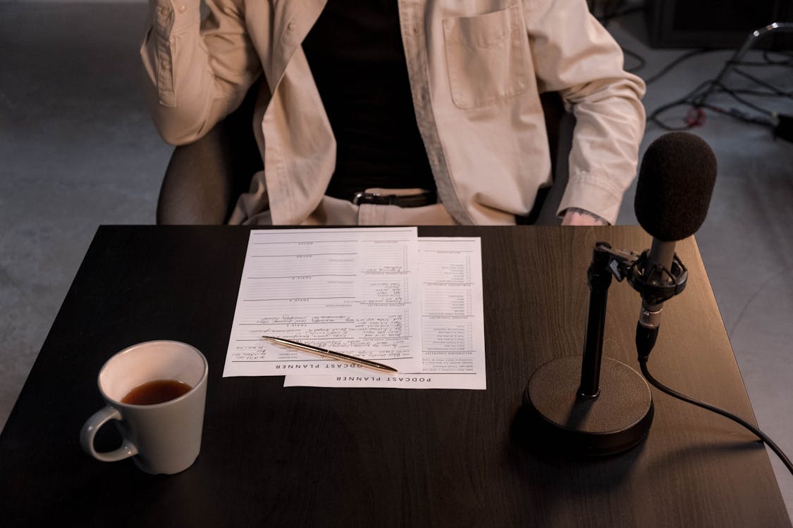 Free Person in White Dress Shirt Sitting Beside Brown Wooden Table With White Ceramic Mug and Black Stock Photo